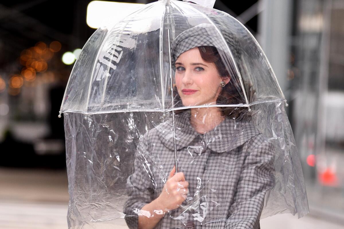 A woman in a vintage suit and hat looks out from under a see-through umbrella.