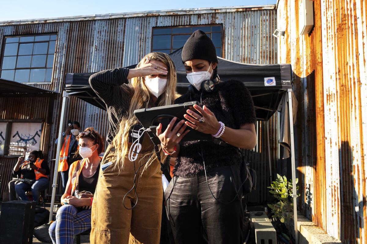 Two women in masks look at a piece of video equipment.