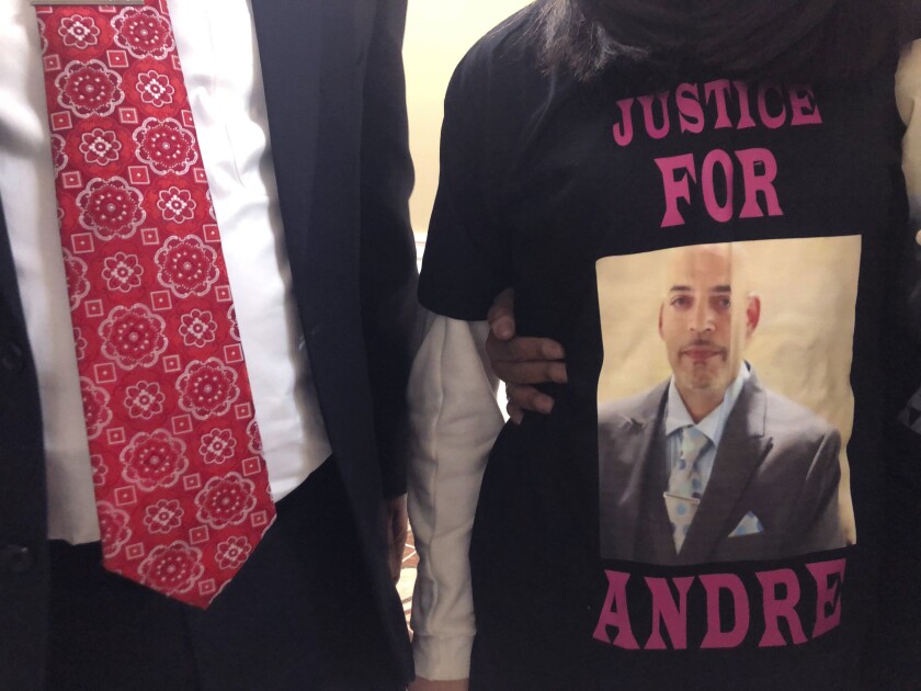 A man in suit and tie stands with a woman in T-shirt showing a man's photo and the words "Justice for Andre."