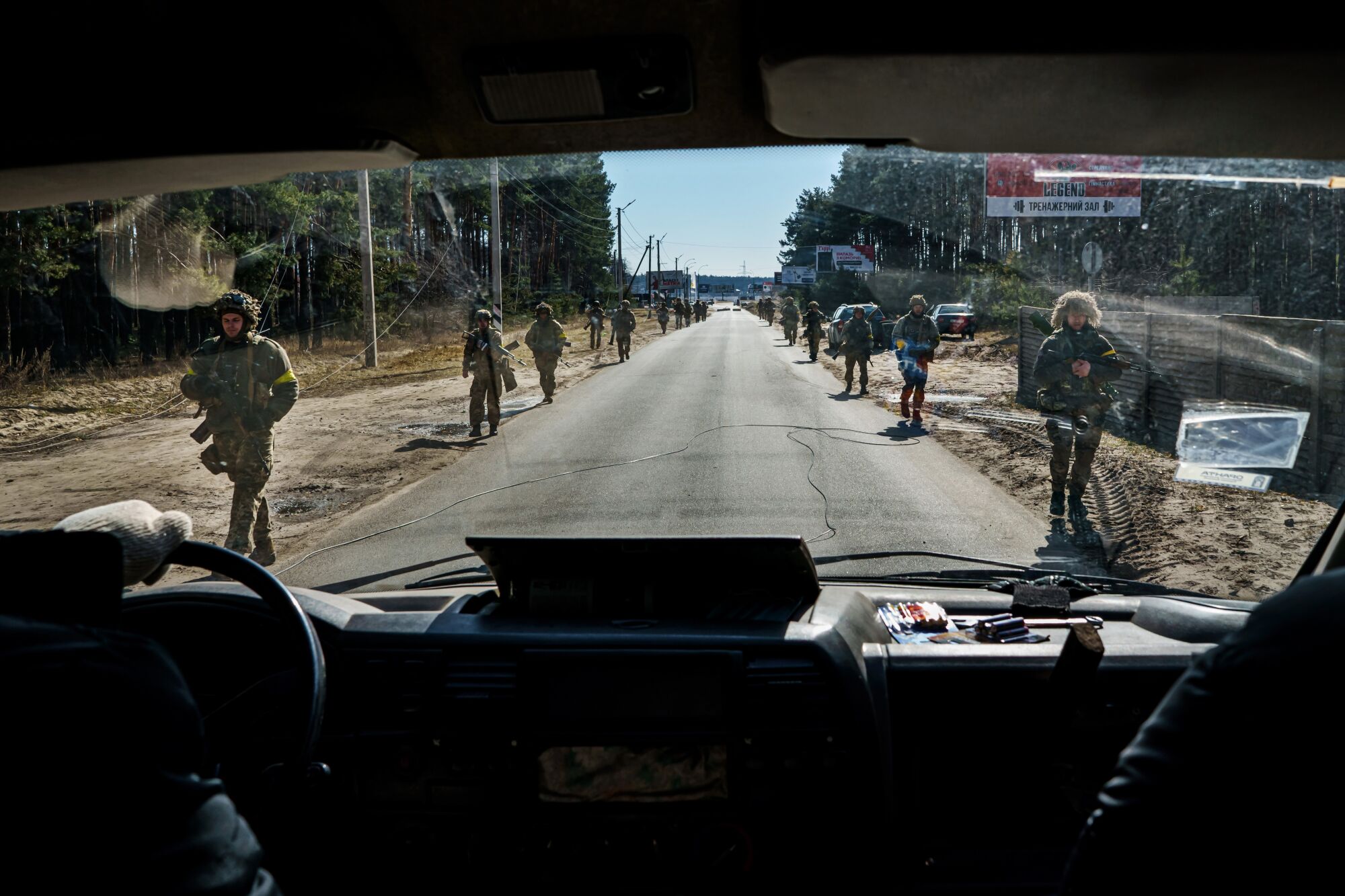 A view through a windshield of armed soldiers marching on either side of the road.