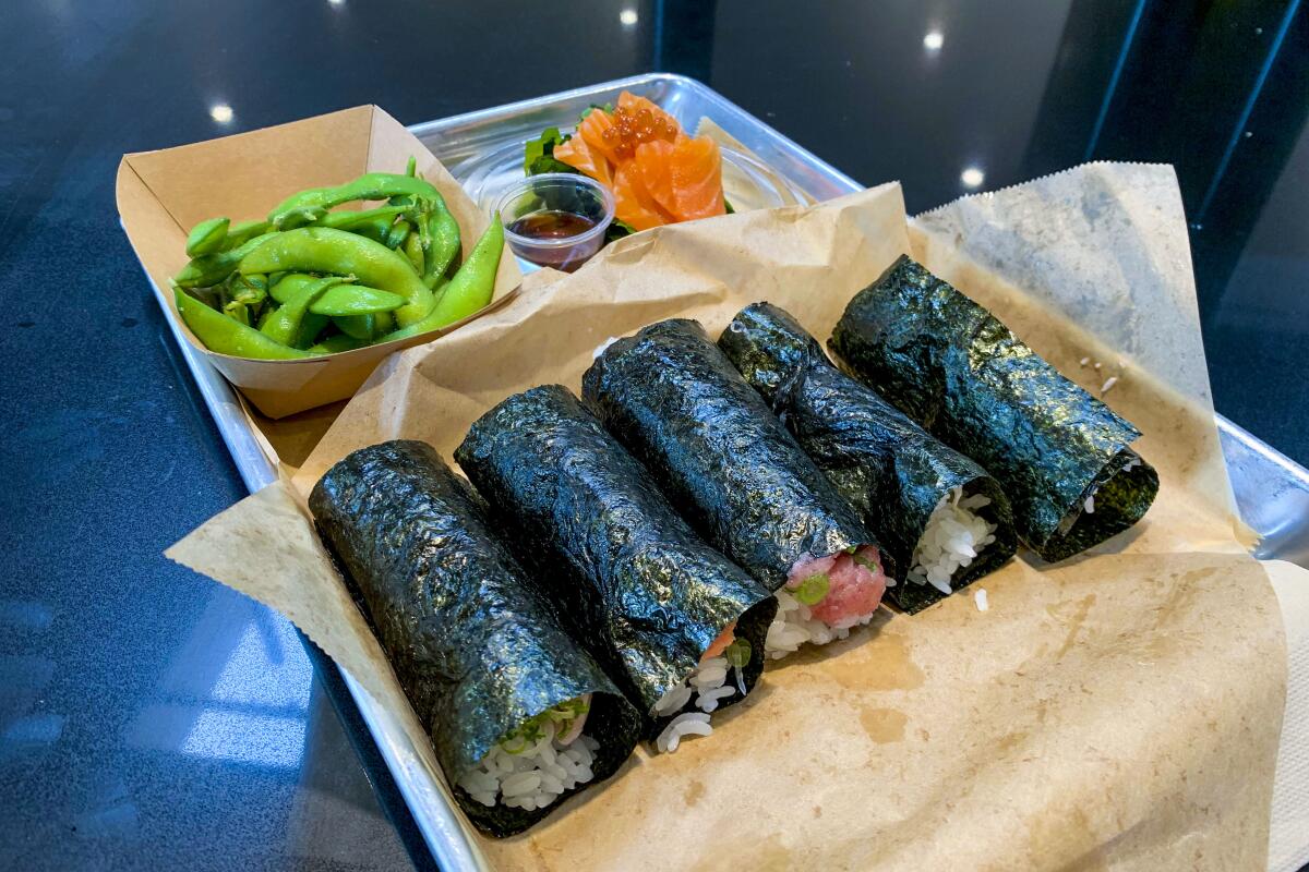 Five hand rolls on a tray with edamame and sliced pickled ginger