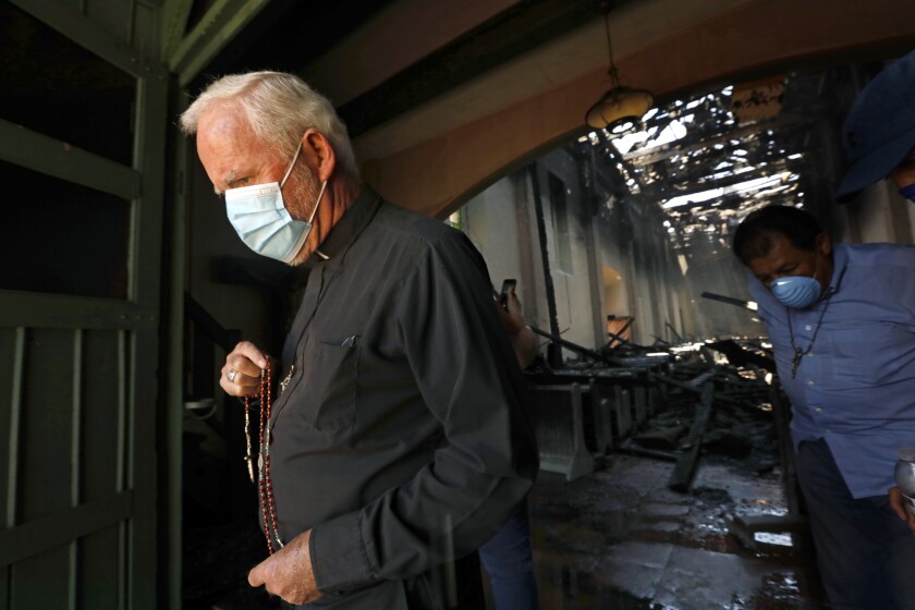Bishop David O'Connell, wearing a mask, walks out of the doors of the burned San Gabriel Mission Church