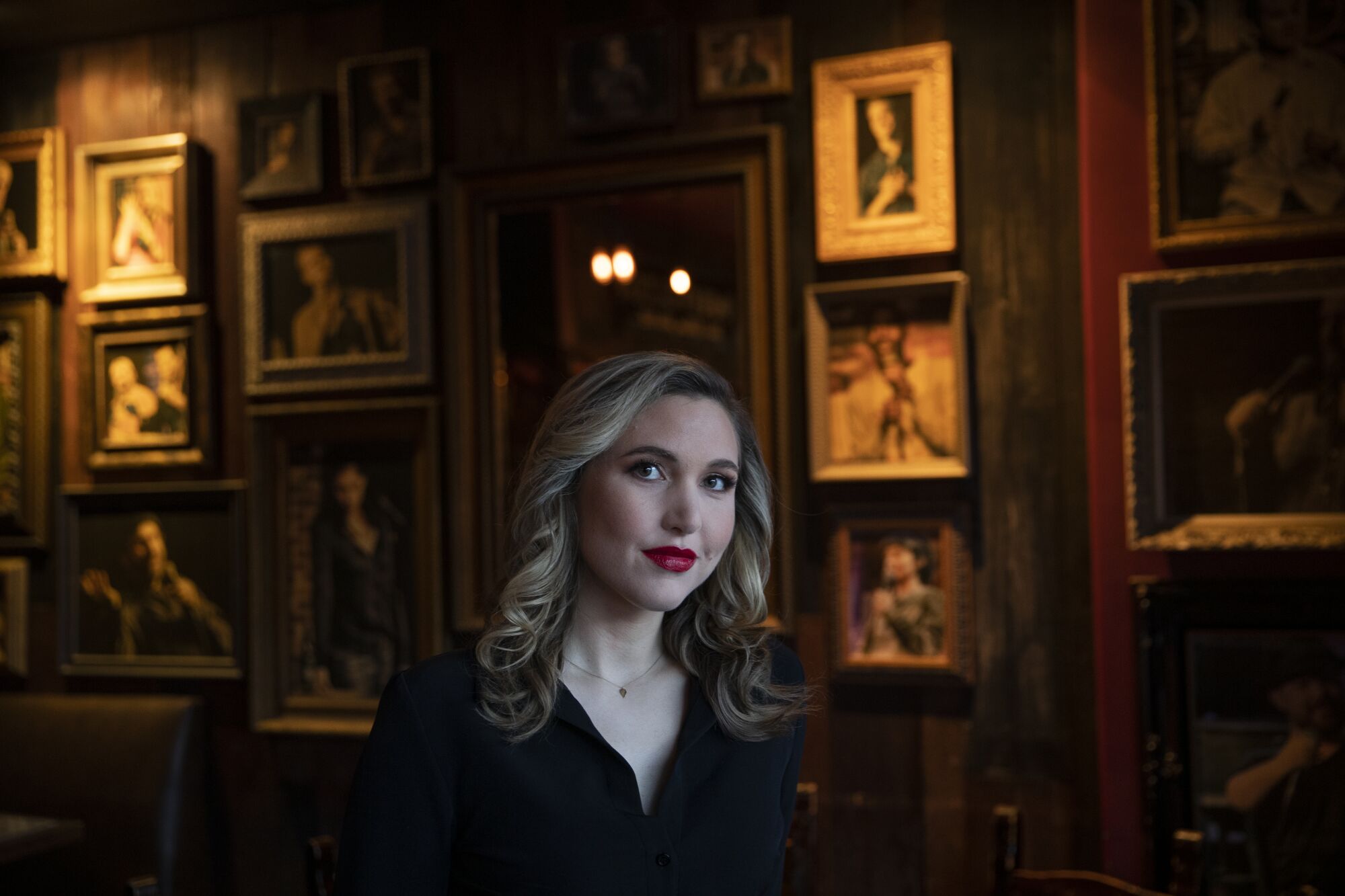Comedian Taylor Tomlinson stands before a wall of framed photos at the Hollywood Improv