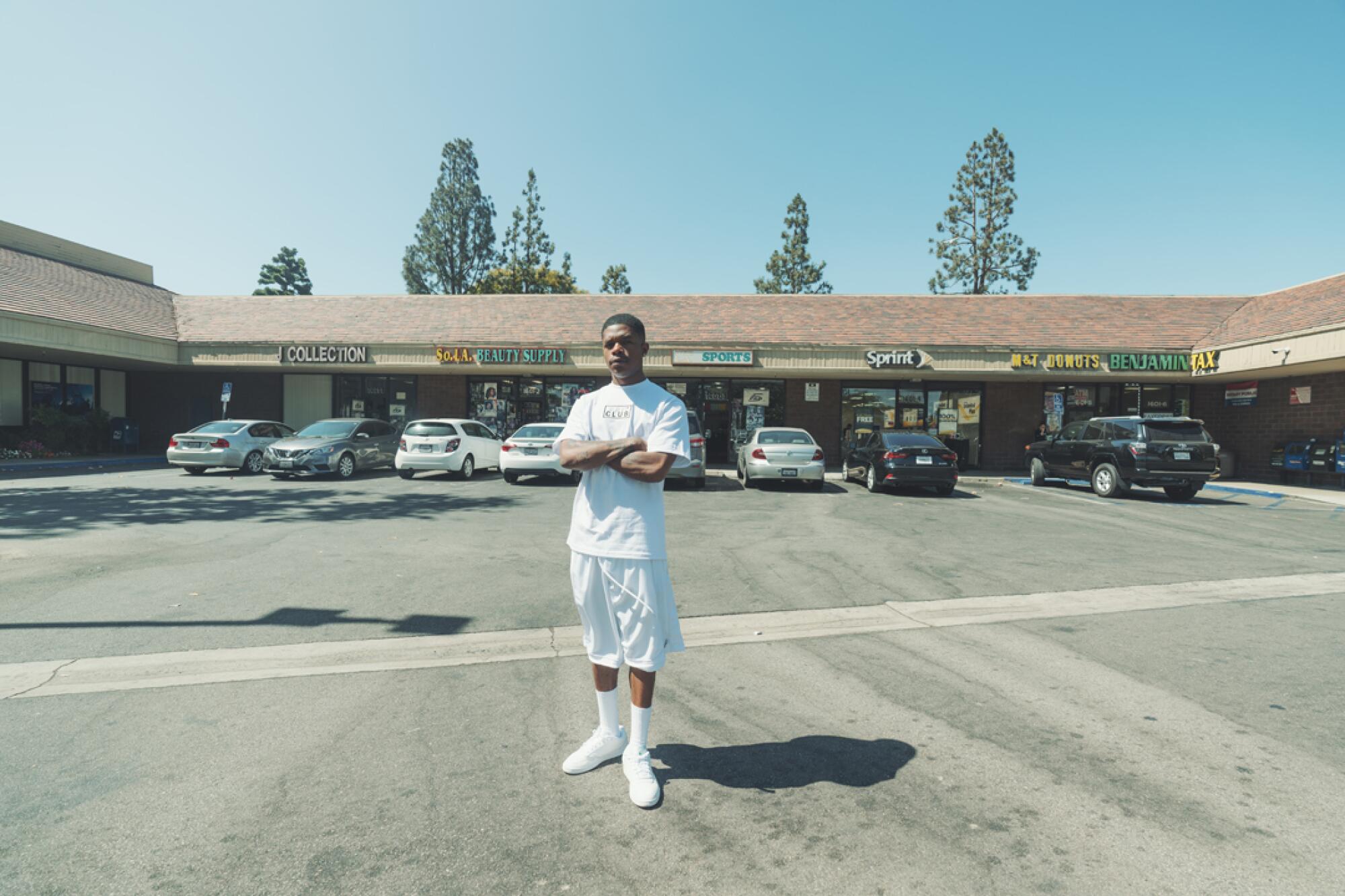 Barrington Darius stands in front of a small plaza wearing a white Pro Club t-shirt, white shorts, socks, and shoes.