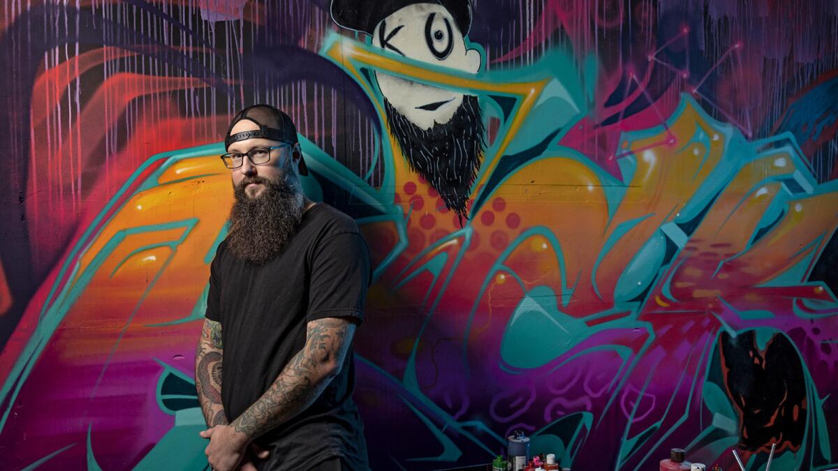 Artist Troy "Kickasso" Cole in front of a mural by artist Jonathan Cirlin, a.k.a. Espy Dpt Znc, at his workshop, Kickasso Kustoms, in downtown Los Angeles.