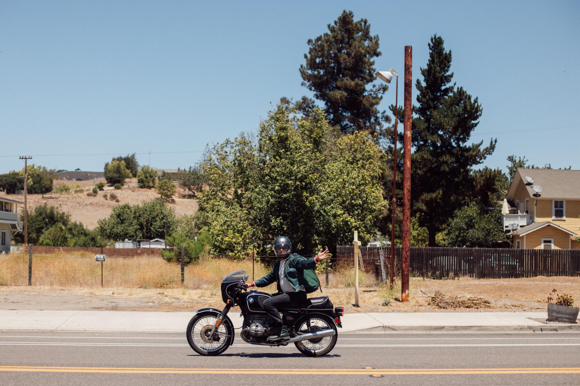 A side view of a biker on the road waving at the camera.