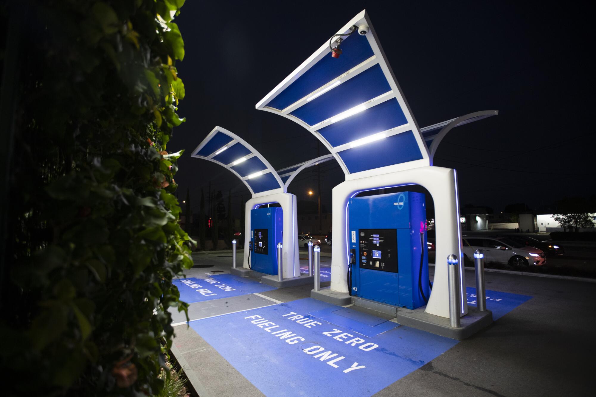 Two fuel pumps at a hydrogen gas fuel station are lit up by lights under a nighttime sky.