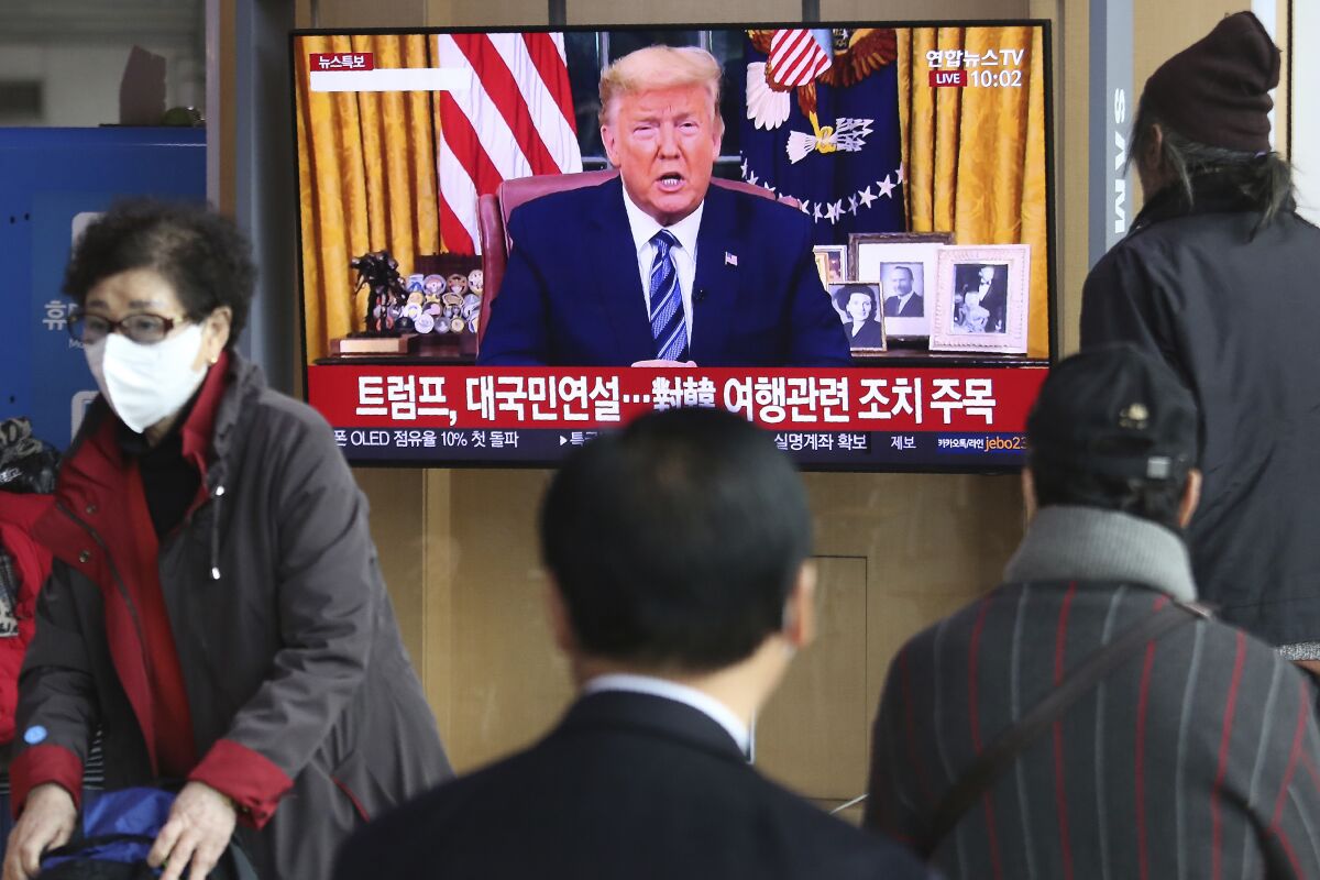 People watch a TV screen showing a live broadcast of U.S. President Donald Trump's speech at the Seoul Railway Station in Seoul, South Korea, Thursday, March 12, 2020. Trump announced he is cutting off travel from Europe to the U.S. and moving to ease the economic cost of a viral pandemic that is roiling global financial markets and disrupting the daily lives of Americans. The Korean letters read: "Trump national speech." (AP Photo/Ahn Young-joon)