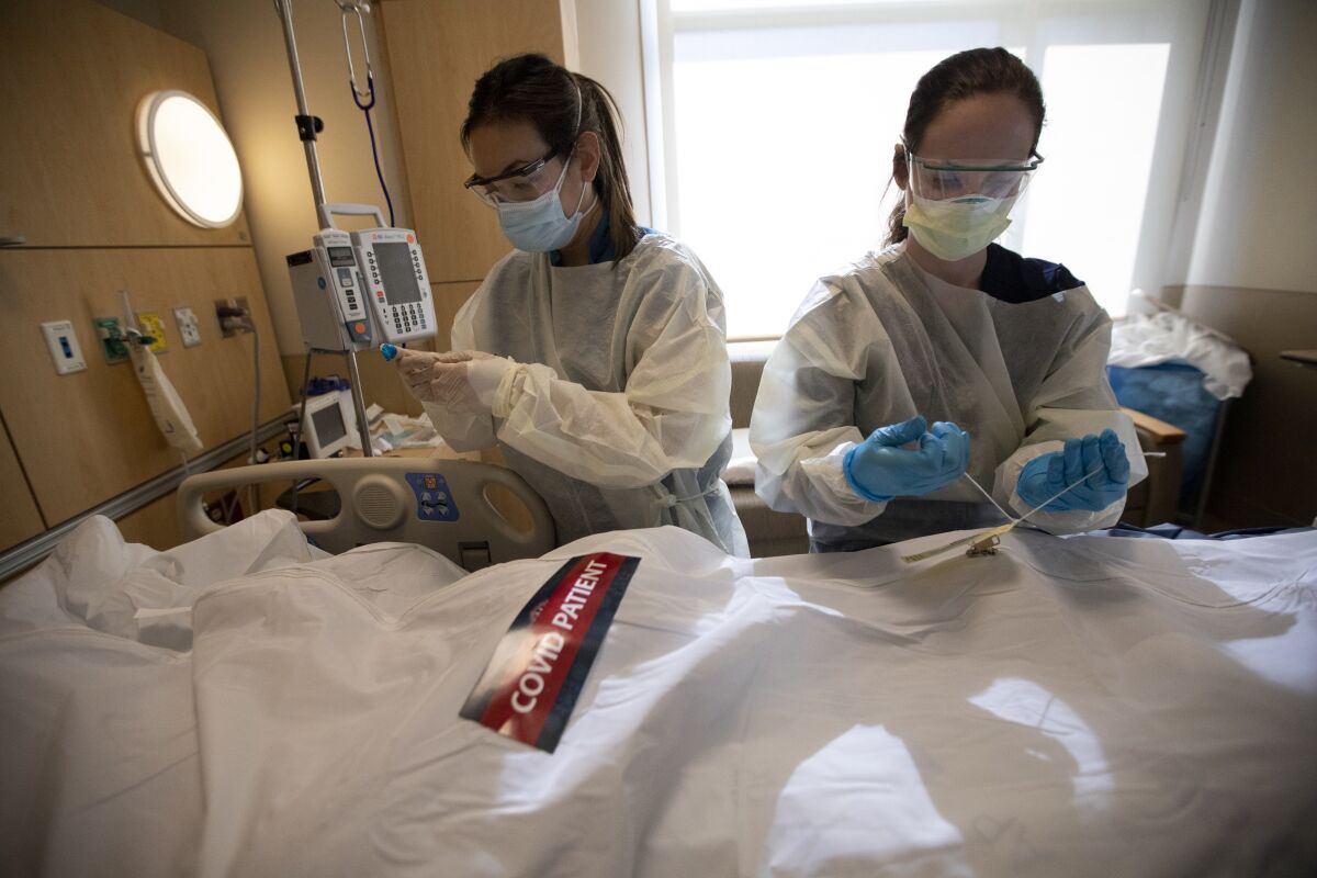 Registered nurses April McFarland, left, and Tiffany Robbins place a body inside a white bag and zip it closed. 