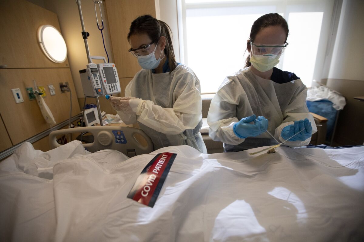 Registered nurses April McFarland, left, and Tiffany Robbins place a body inside a white bag and zip it closed.