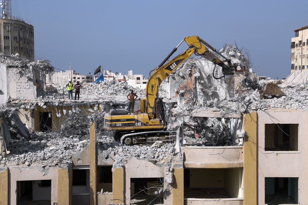 Palestinian workers use a backhoe to break and remove parts of the Al-Jawhara building, that was damaged in Israeli airstrikes during Israel's war with Gaza's Hamas rulers last May, in the central al-Rimal neighborhood of Gaza City, Nov. 16, 2021. The Gaza Strip has few jobs, little electricity and almost no natural resources. But after four bruising wars with Israel in just over a decade, it has lots of rubble. Local businesses are now finding ways to cash in on the chunks of smashed concrete, bricks and debris left behind by years of conflict. (AP Photo/Adel Hana)