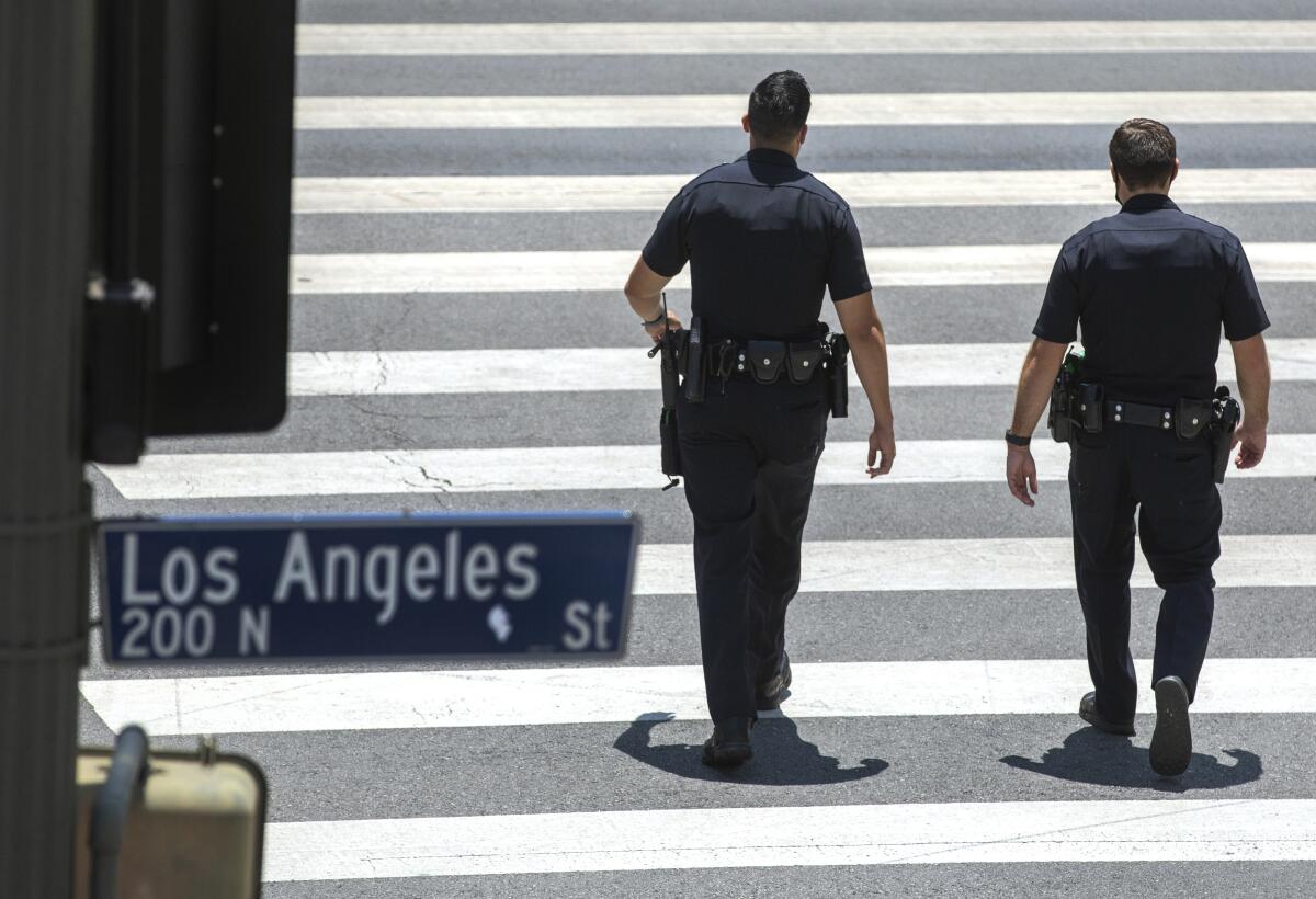 Two police officers walk away from the camera, walking on a cross walk. 