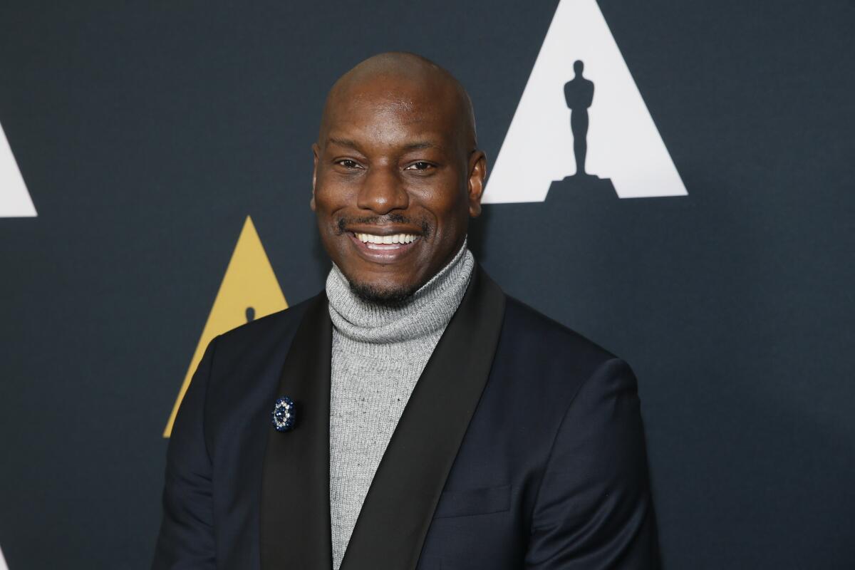 Tyrese Gibson wears a gray turtleneck sweater and a black blazer while posing for photos at a red carpet event