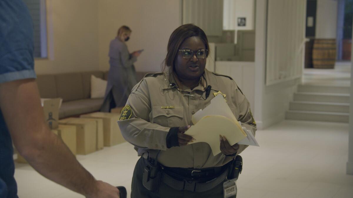 A courtroom bailiff holds a folder full of papers in a scene from "Jury Duty."