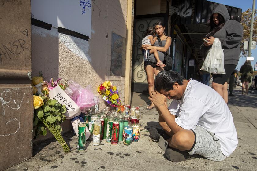 LINCOLN HEIGHTS, CA -SEPTEMBER 12, 2022: Elvis Mejia pays his respects at a memorial on Broadway in Lincoln Heights for his nephew Javier Mejia, 17, one of two teenage boys who were shot and killed Sunday night at a street carnival in Lincoln Heights. In background, left is his wife Aide Rivera, holding their daughter, Heidi Mejia, 2. (Mel Melcon / Los Angeles Times)