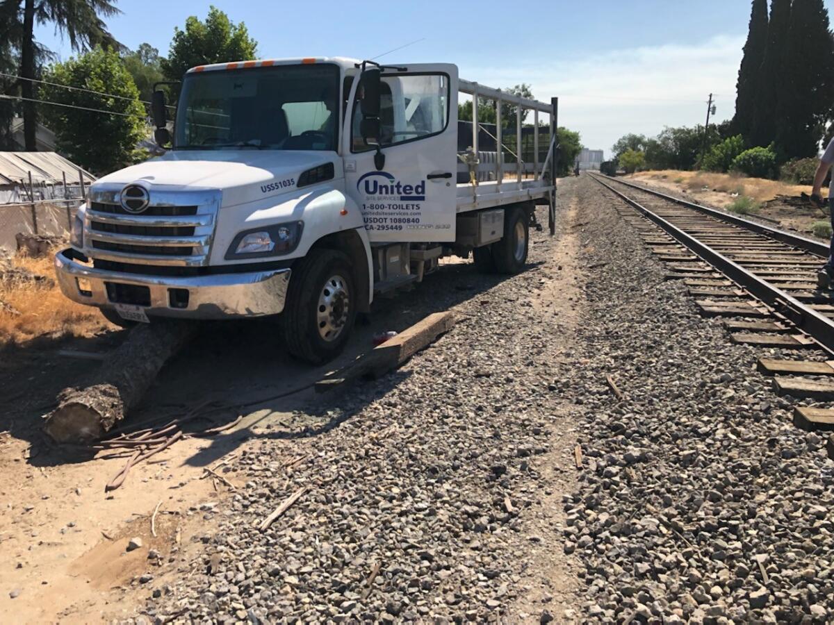 A truck with a door open sits next to railroad tracks.