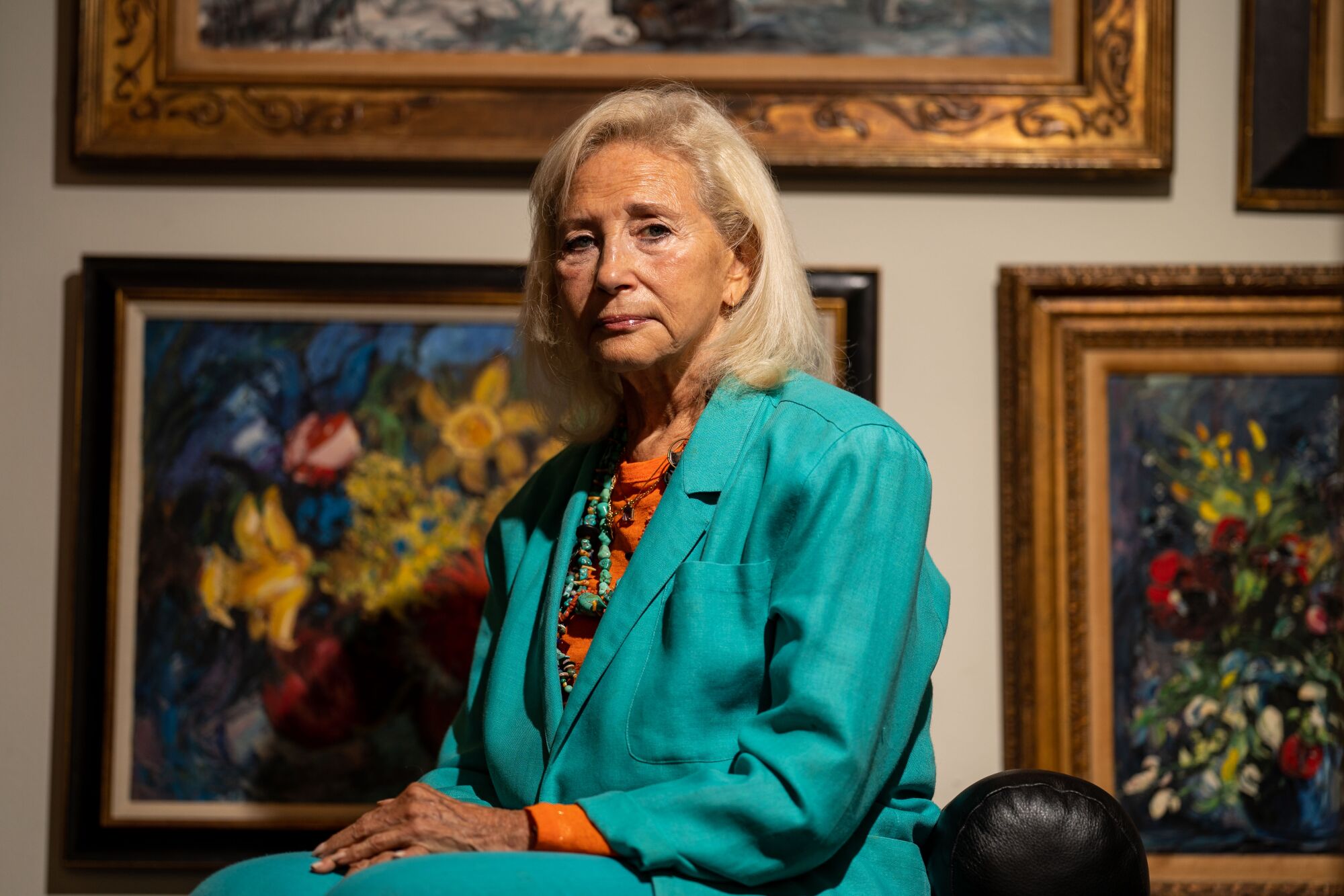 A woman sits for a portrait with paintings as a backdrop.