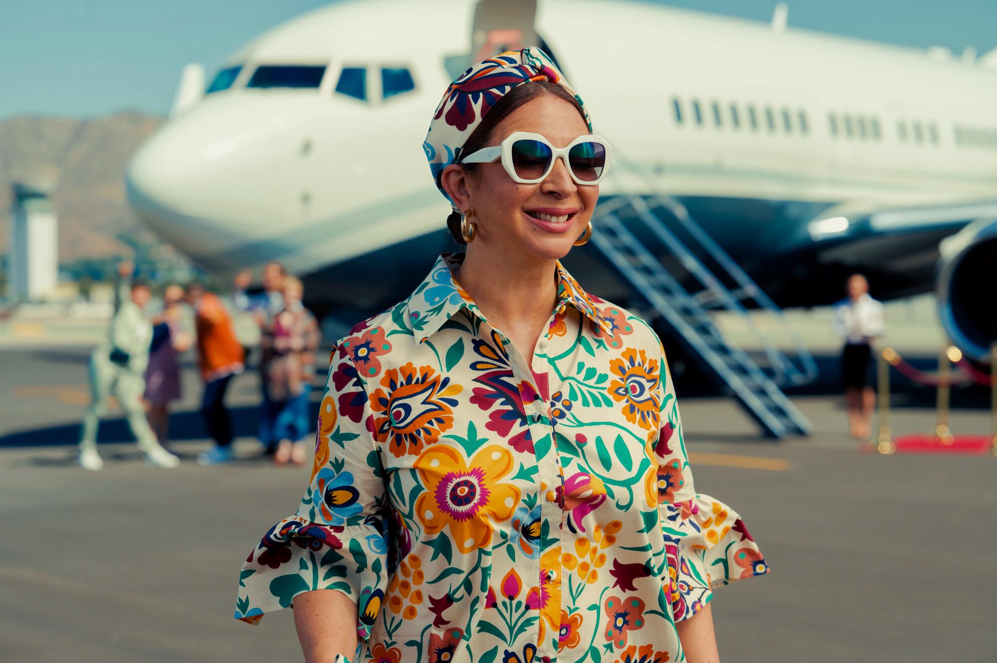 Maya Rudolph walks on the tarmac with a jet in the background in "Loot." 