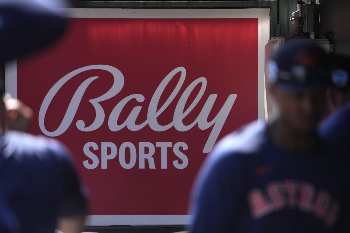Houston Astros players walk in front of a Bally Sports sign in the dugout.
