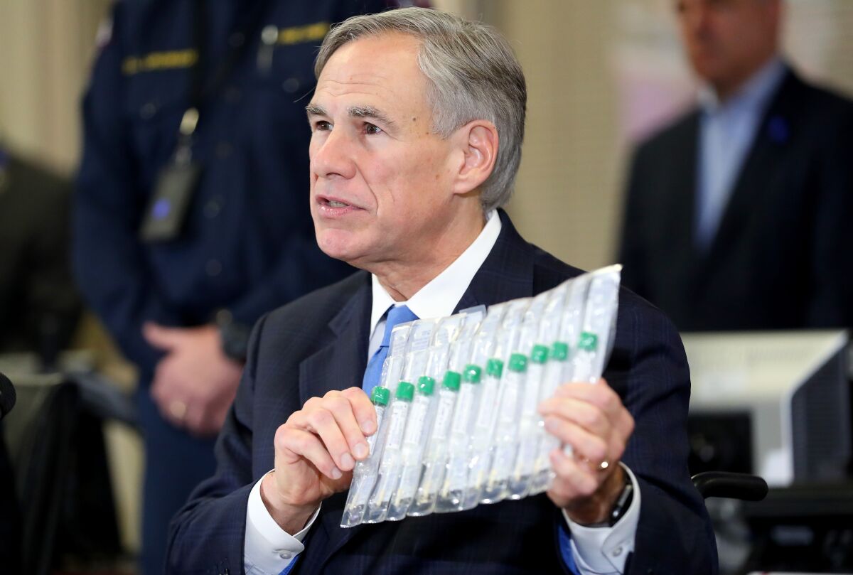 Texas Gov. Greg Abbott, holding test vials in mid-March, has announced plans to ease some restrictions. More than 400 people in Texas have died of COVID-19.