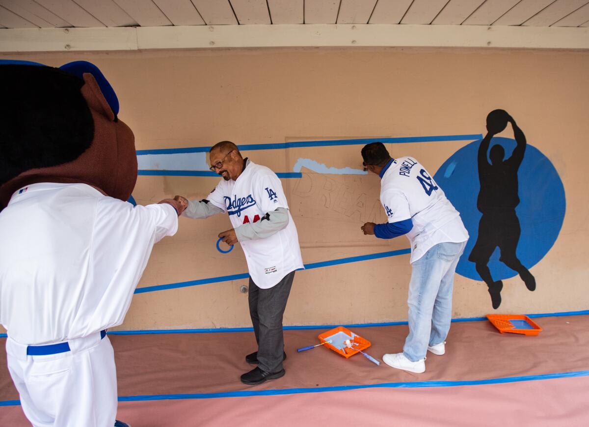 Former Dodgers outfielder Ken Landreaux bumps fists with the Dodgers mascot while ex-Dodgers pitcher Dennis Powell paints a mural on Monday in Westchester.