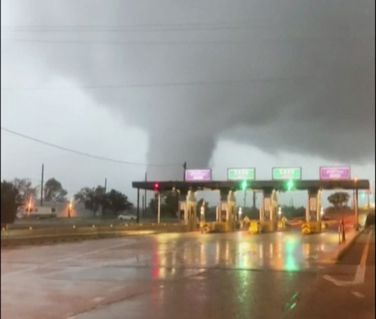 The funnel of a large tornado is seen behind a roadway slick with rain.
