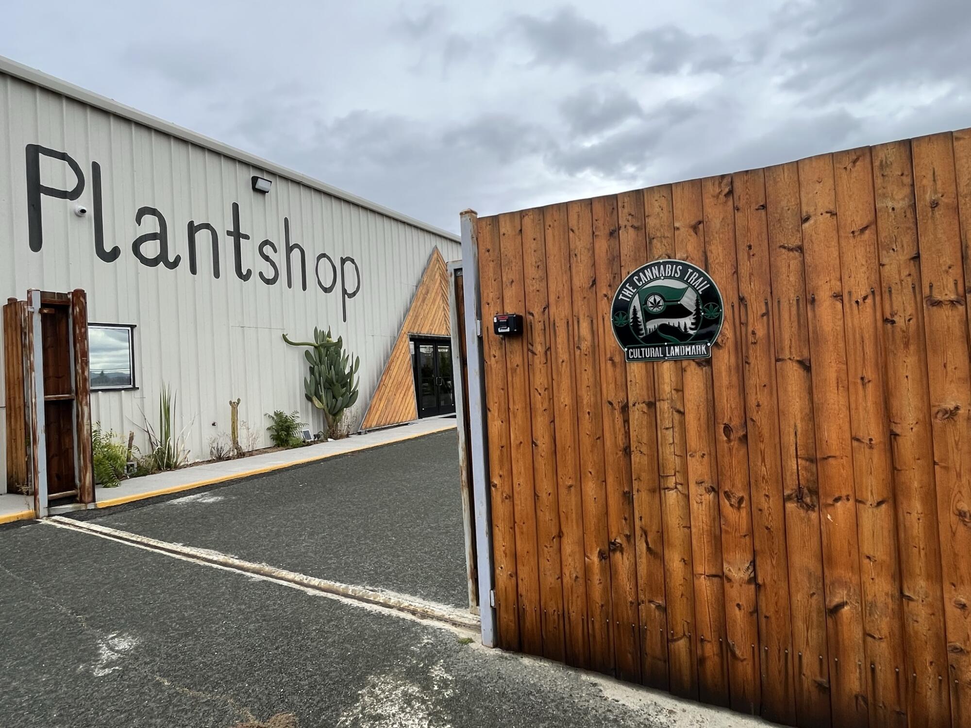 A building with the word Plantshop next to a wooden fence with a green and black plaque on it