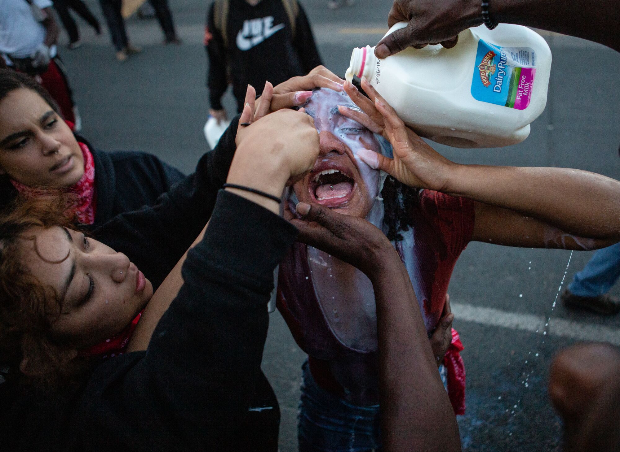 Two people help a protester, pouring milk over her eyes as she cries out.
