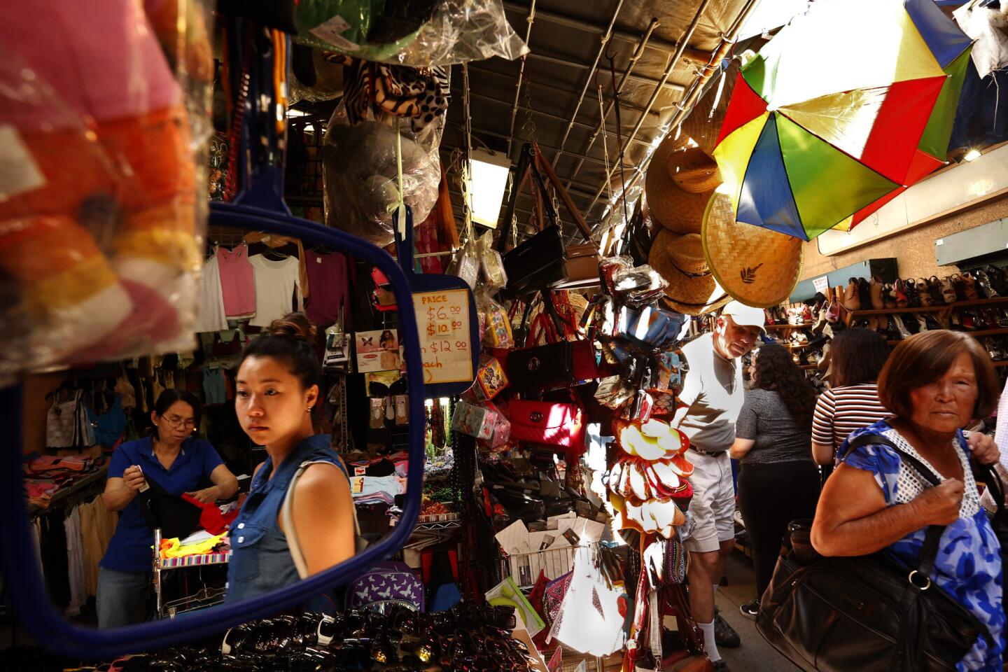 Shoppers are caught in a mirror as others make their way through the swap meets at Saigon Plaza in Chinatown. There are many changes coming to Chinatown including wine bars, fancy office space, art galleries that could alter the future of the swap meets.