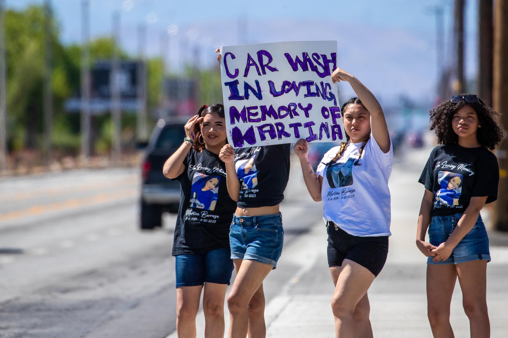 Four teenage girls stand on a roadside holding a hand-painted sign that says "Car wash in loving memory of Martina"