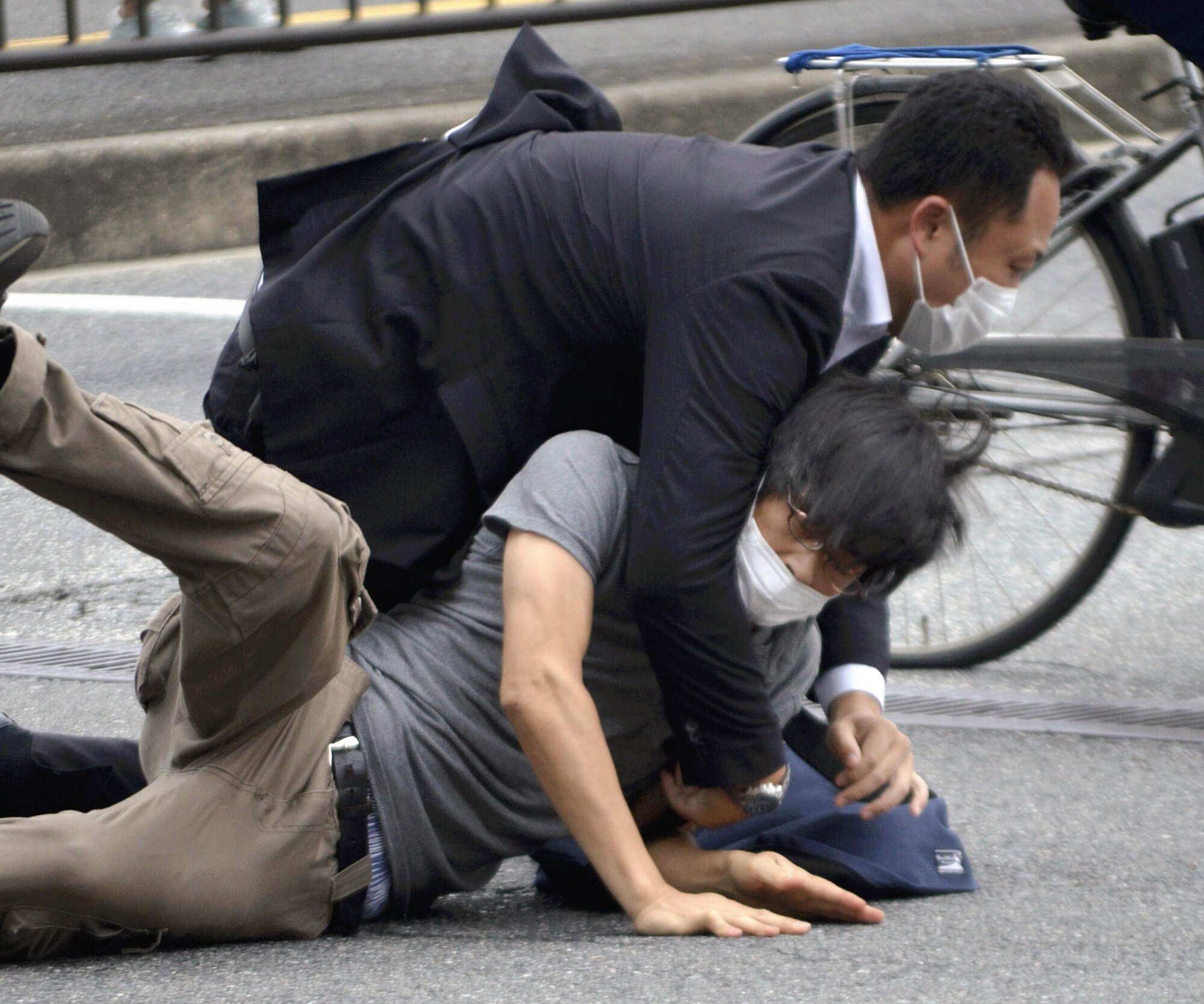 Tetsuya Yamagami, bottom, is detained near the site of gunshots in Nara Prefecture, western Japan, Friday