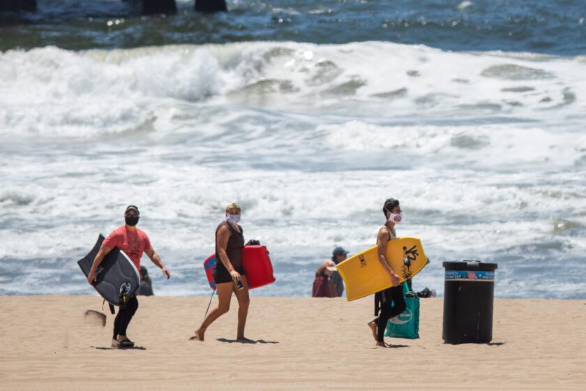 MANHATTAN BEACH, CA - MAY 15: People walks with boogie boards and face masks on the beach in Manhattan Beach, CA, Friday, May 15, 2020, during the coronavirus pandemic. (Jay L. Clendenin / Los Angeles Times)