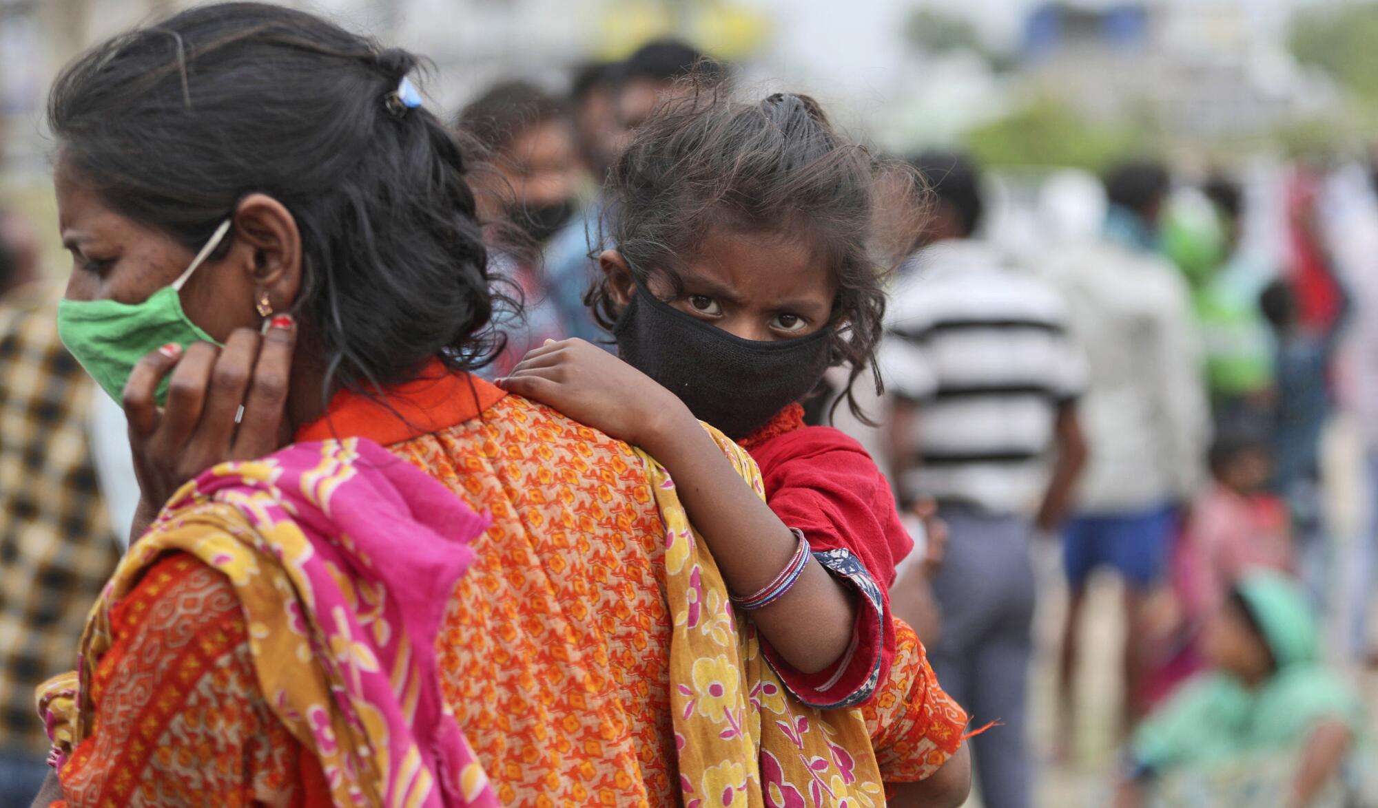 A woman carries a child as they wait with other migrant worker families to have their temperatures checked in Jammu, India.