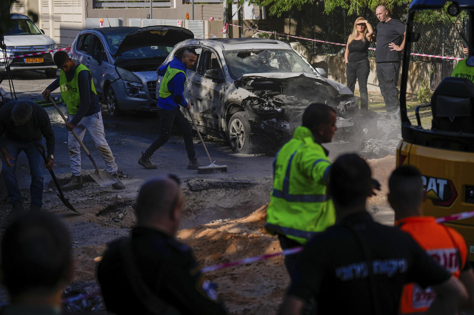People look at damage to cars and pavement in an Israeli street.