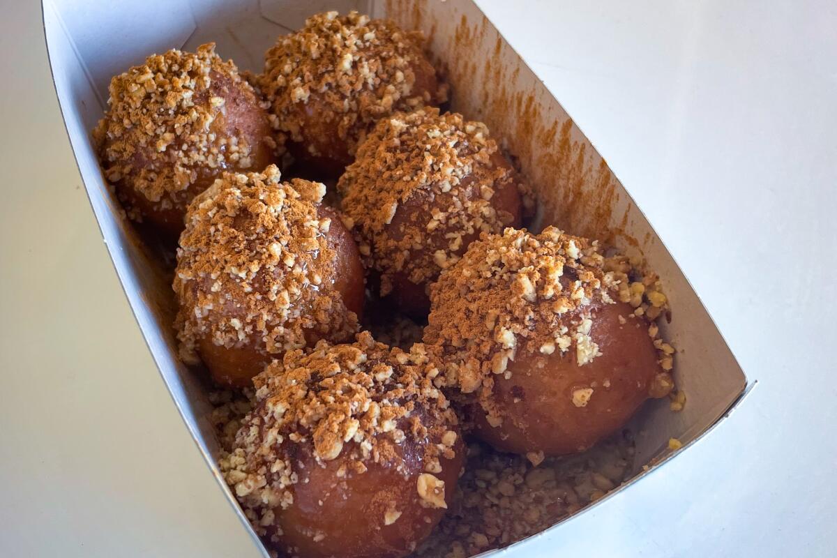 Six nut-topped doughnut holes in an open cardboard dish