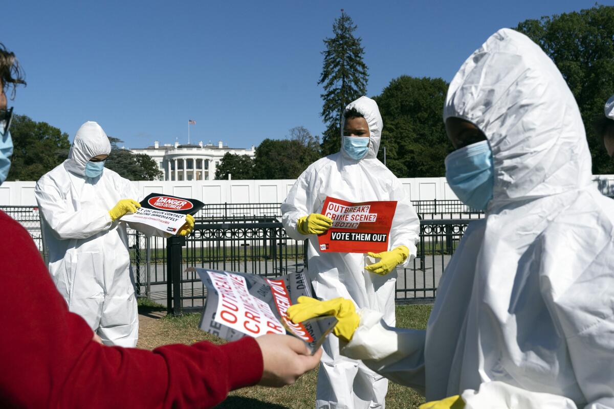 Protesters wearing full-body PPE hold signs outside the White House 