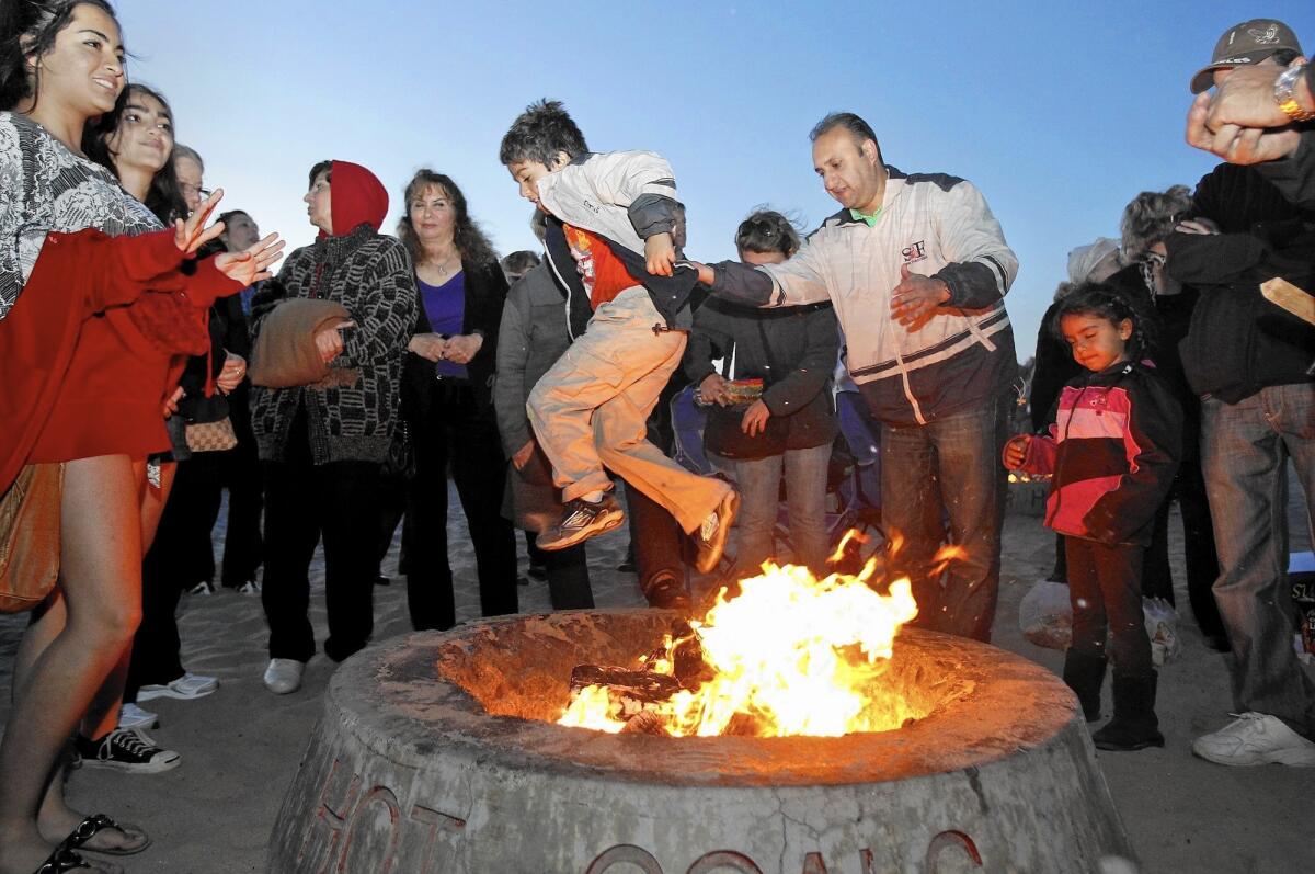 Kianoush Hamadani, center right, of Irvine helps his son Cameron over a bonfire in celebration of the Persian New Year, known as NowRuz, in 2012.