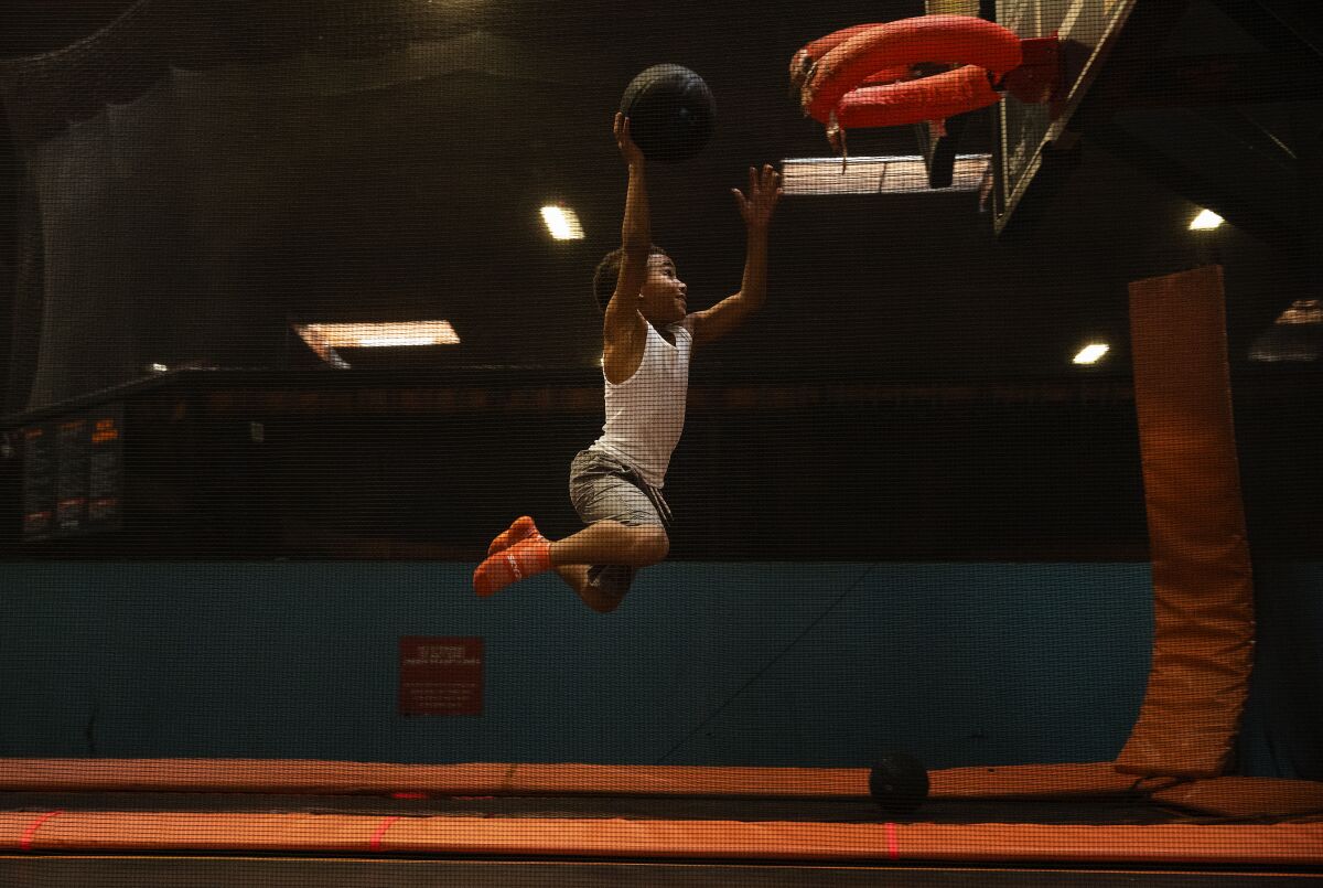 A boy tries to dunk a basketball after jumping on a trampoline.