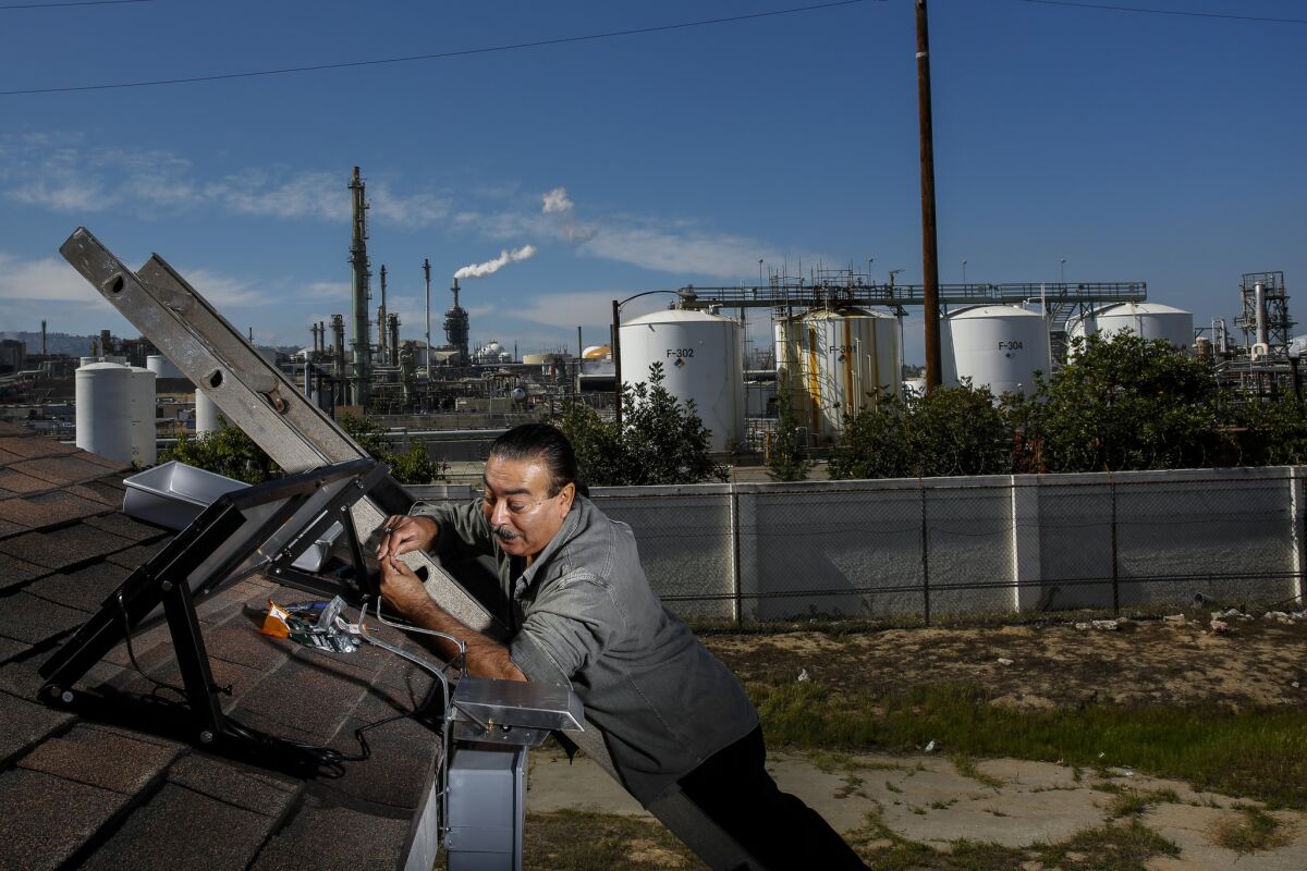 Jesse Marquez, executive director of Coalition for a Safe Environment, installs an pollution-monitoring device on a Wilmington home near the Phillips 66 oil refinery.