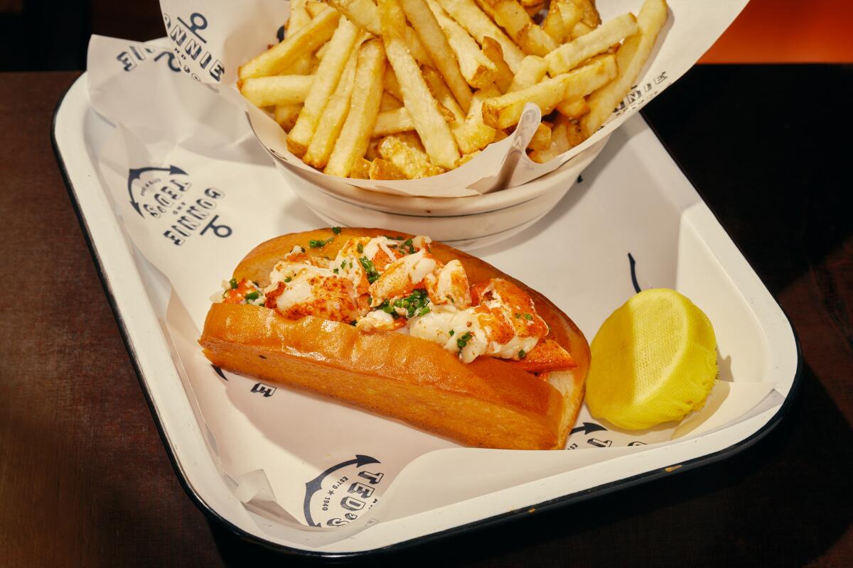 A lobster roll sits in a container with fries and half of a lemon.