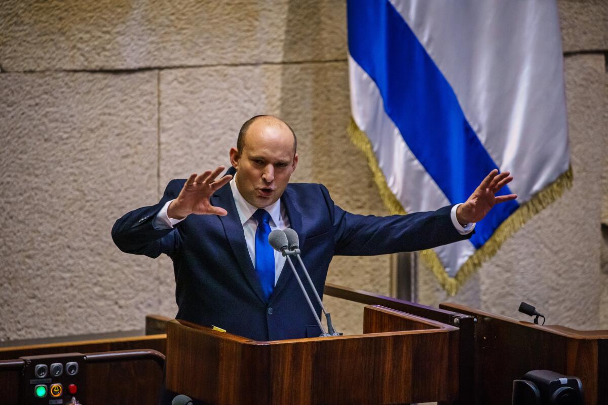 Naftali Bennett with his arms raised at a lectern in the Knesset. 