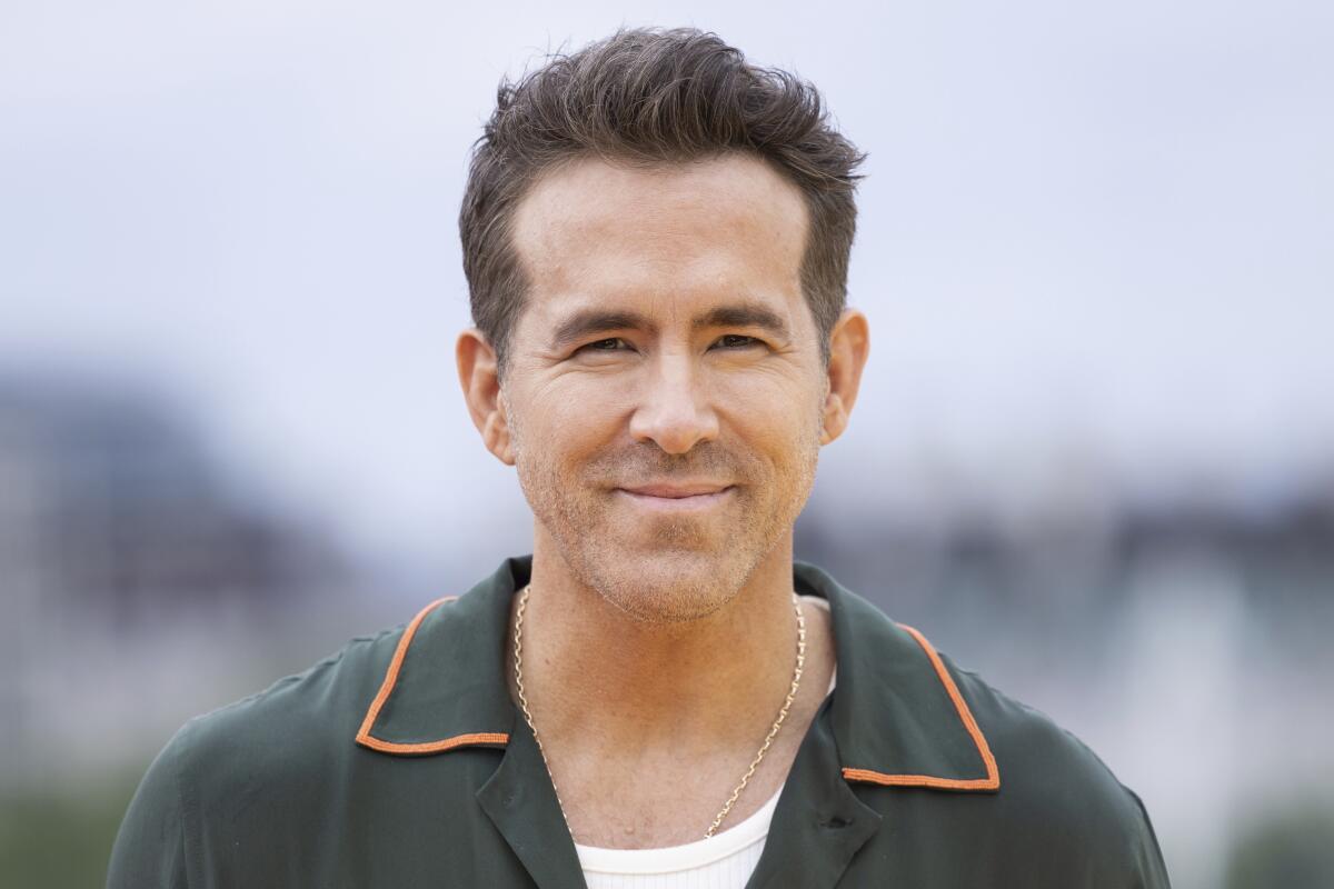 Ryan Reynolds grinning with his mouth closed and wearing a green shirt with a collar