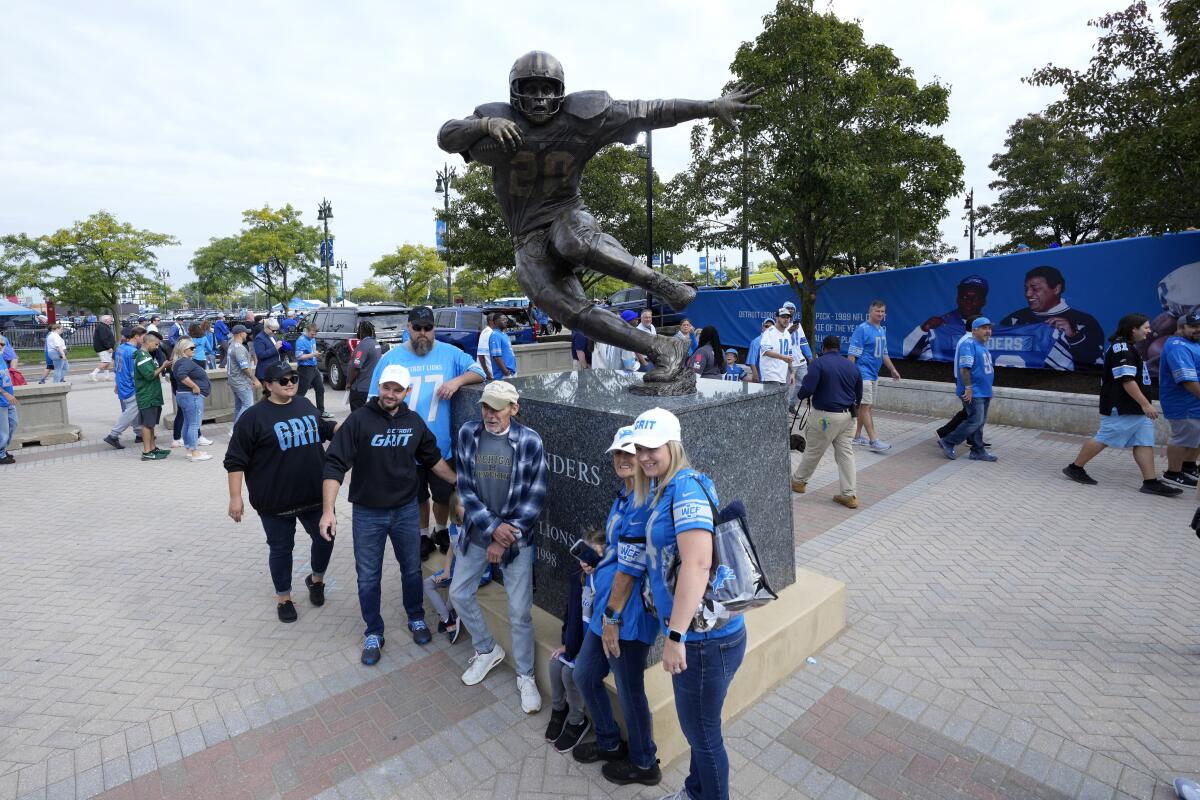 Fans pose for a photo in front of a statue of former Detroit Lions running back Barry Sanders before a 2023 game. 