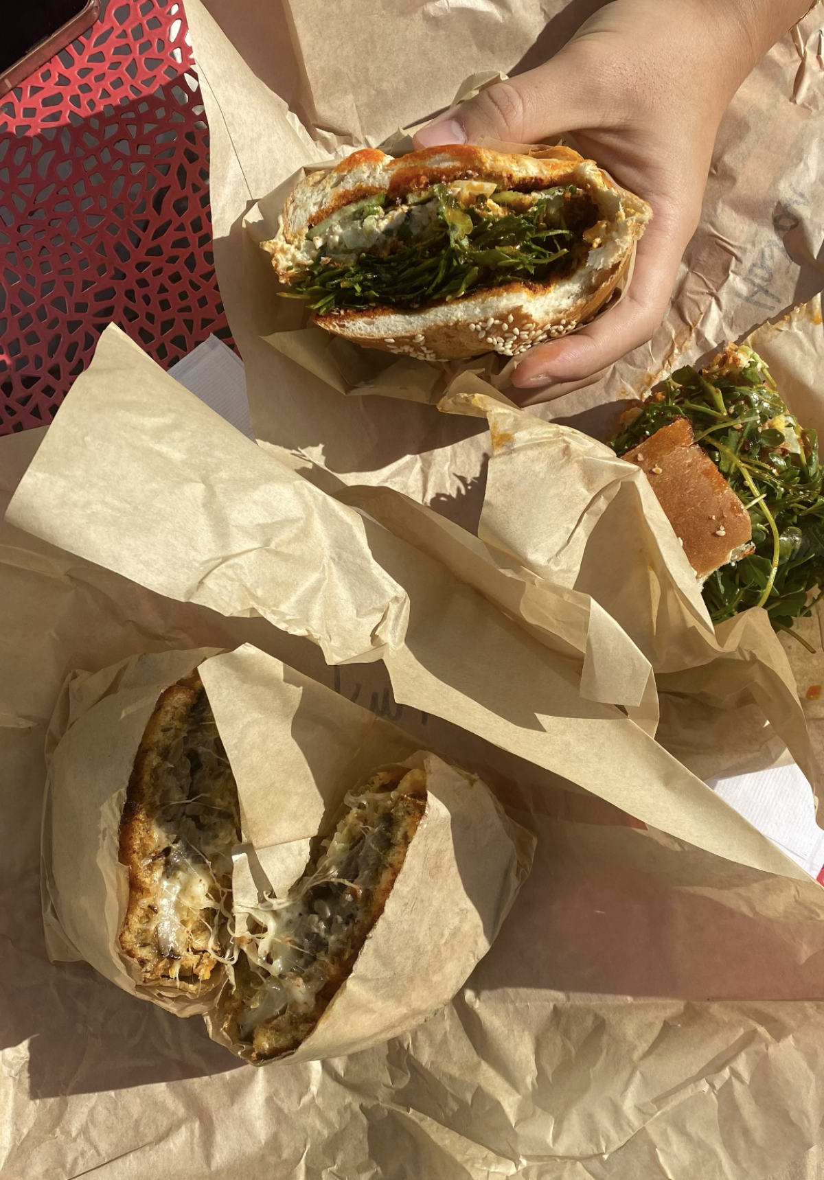 A hand holds a Jeff's Table sandwich over brown butcher paper on a table outside.