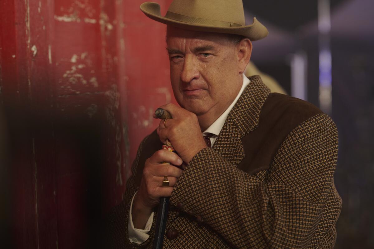 An older man in a suit and hat smokes a cigar in the movie "Elvis."
