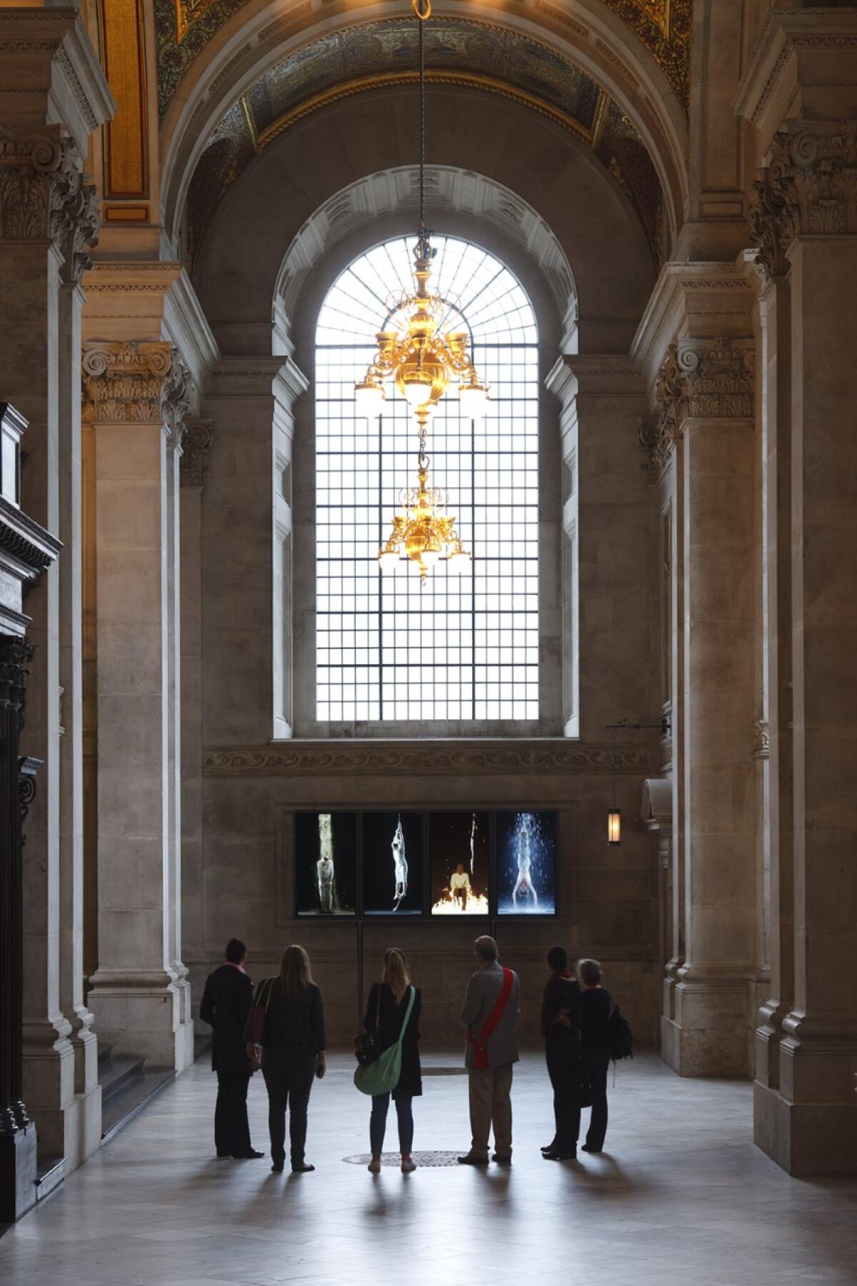 Patrons look at an installation at a church that shows human personifications of earth, air, fire and water.