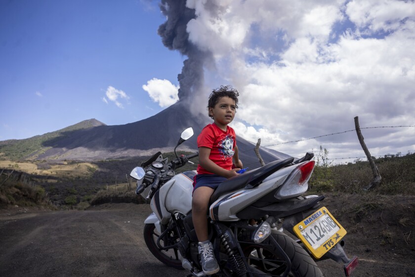 A child sits on a motorcycle as the Pacaya volcano erupts in the background, viewed from San Vicente Pacaya, Guatemala, Wednesday, March 3, 2021. (AP Photo/Santiago Billy )