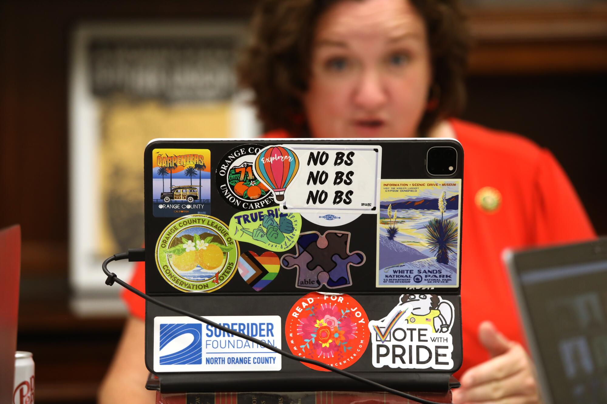  Rep. Katie Porter sitting behind a laptop covered in a variety of travel and issue stickers, one reading simply, "No BS"