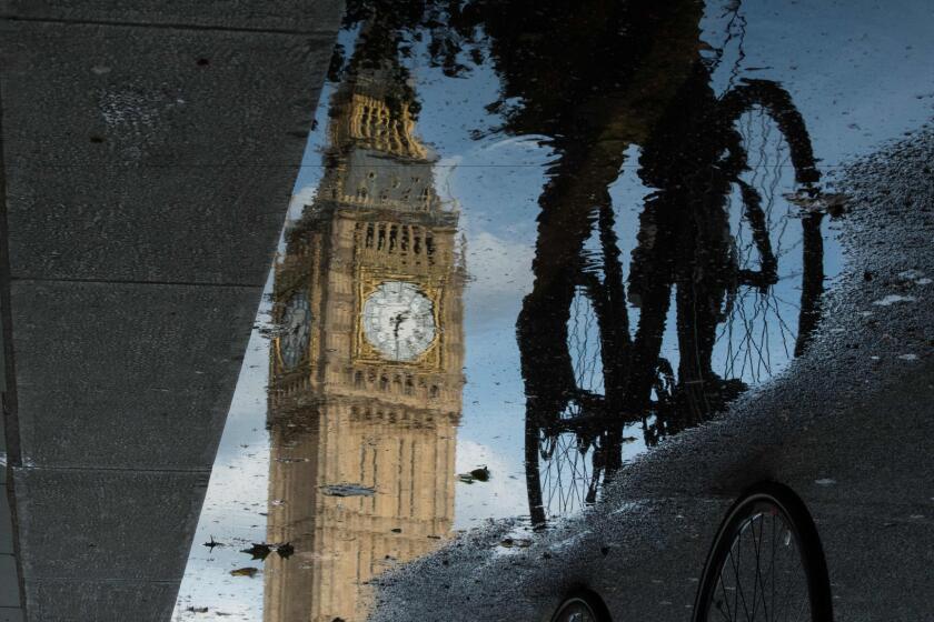 Big Ben is reflected in a puddle as a cyclist rides by.