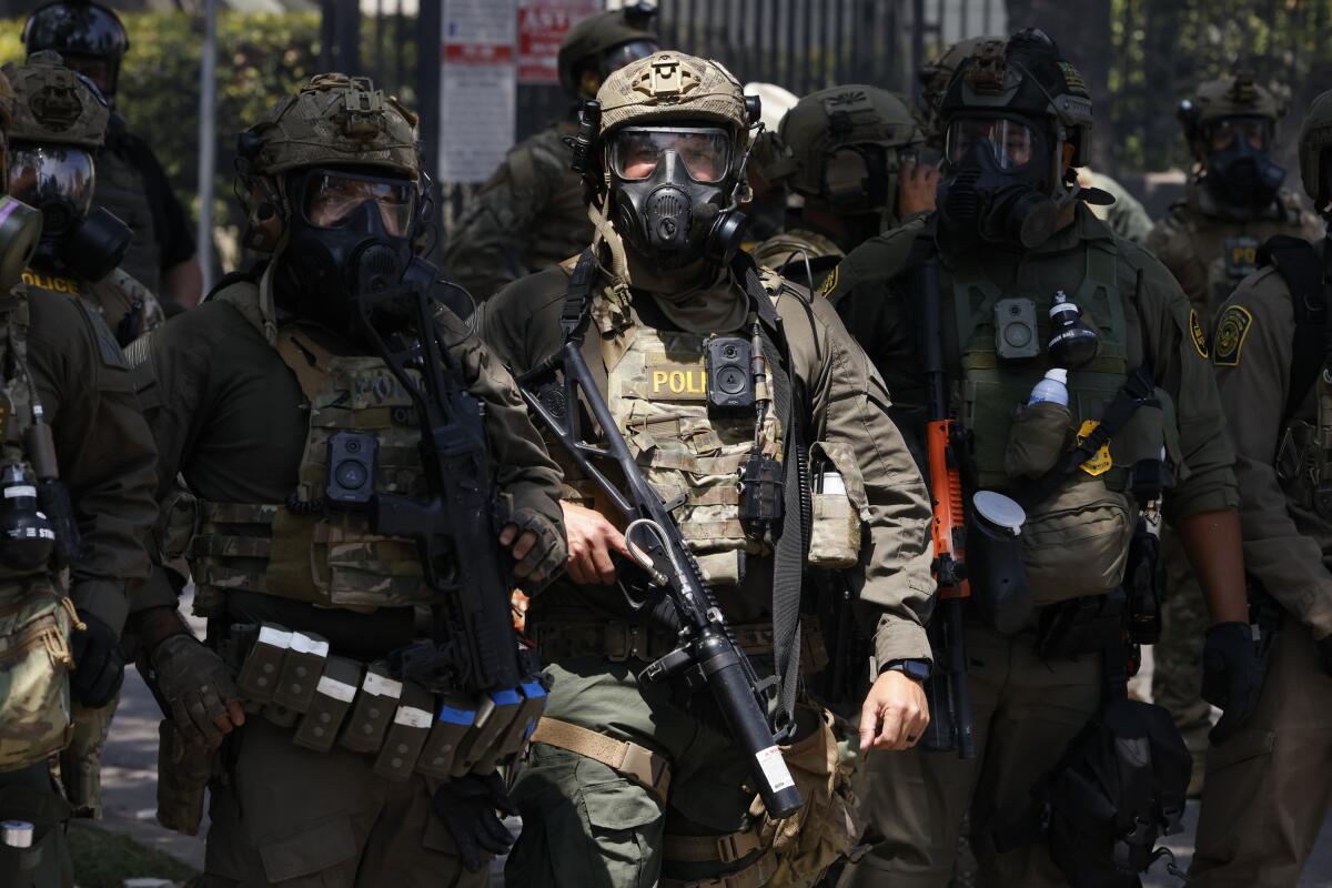 ICE officers wear helmets and gas masks.